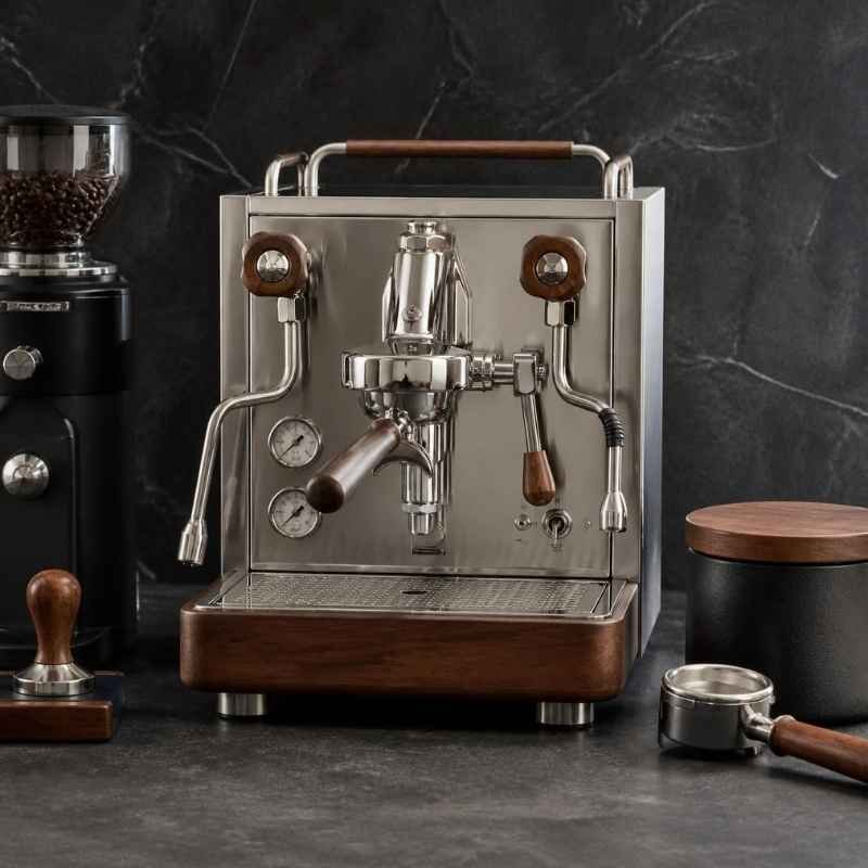 A high-end stainless steel espresso machine with walnut wood accents on a dark slate countertop for coffee gear reviews.
